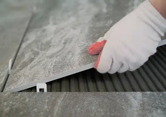 Des mains avec des gants en train de poser du carrelage grand format