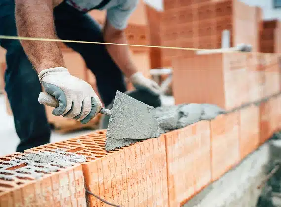 Un homme en train de mettre du ciment sur des briques d'une maison en construction